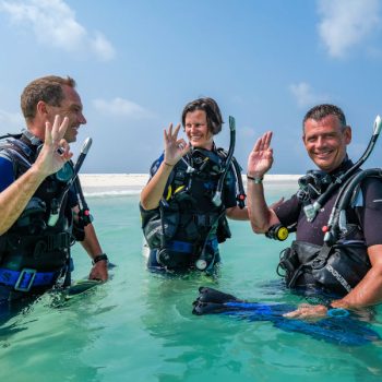This pictures shows three divers in the water conducting a pre dive safety check before an open water dive. This is part of the PADI or SSI open water diver course